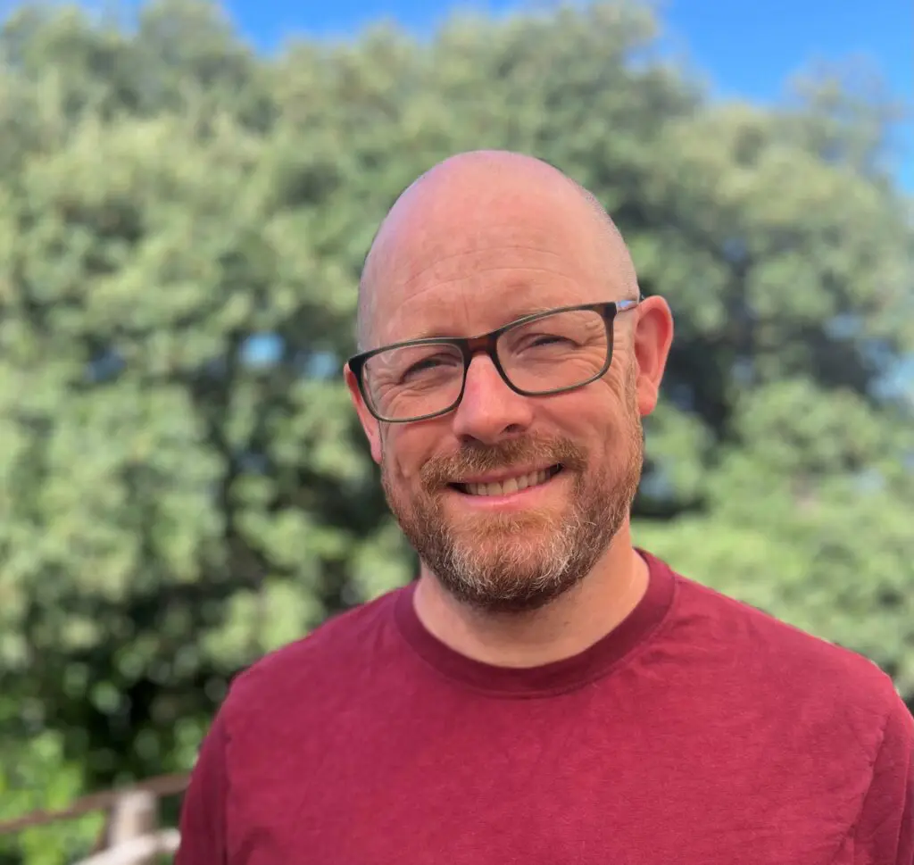Photo of a smiling man with glasses against a background of trees
