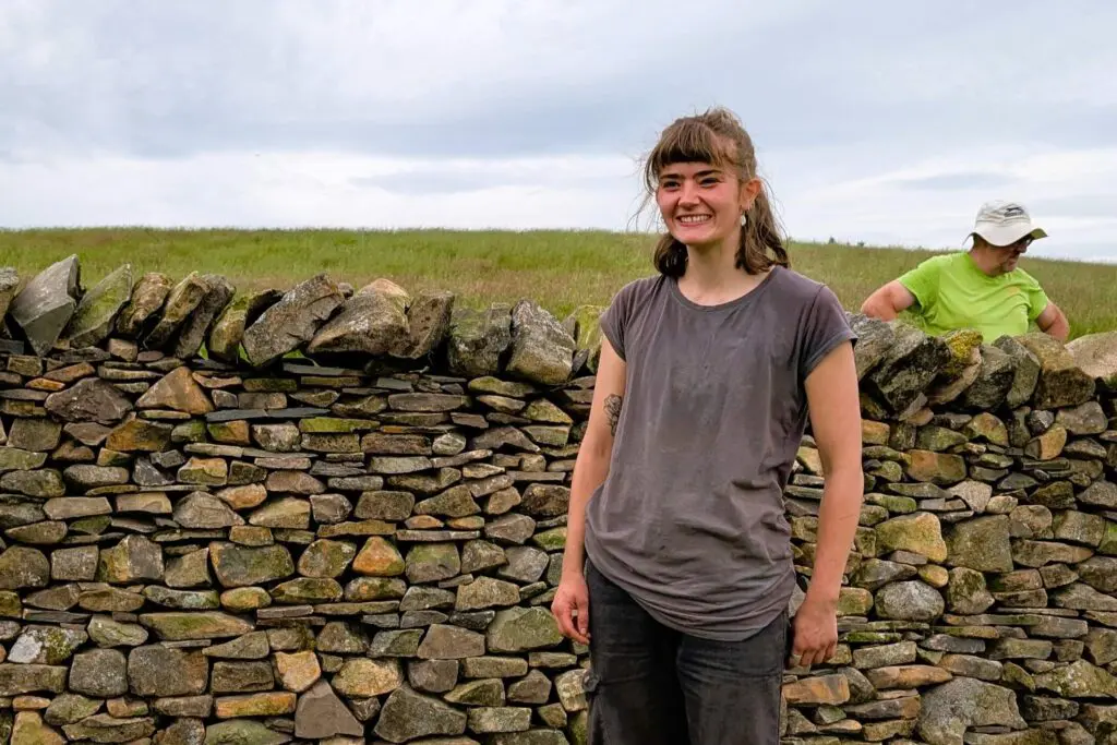 A young woman by a dry stone wall