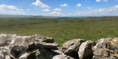 View over a dry stone wall into a lovely green field and a tarn beyond