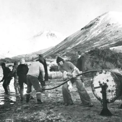 An old photo of people puling a cable and laying it under a lake