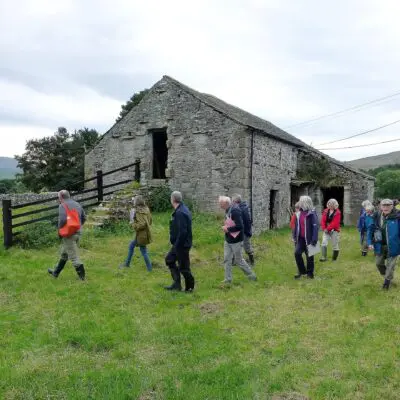 People walking past an old farm building