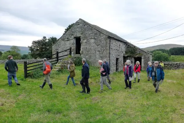 People walking past an old farm building