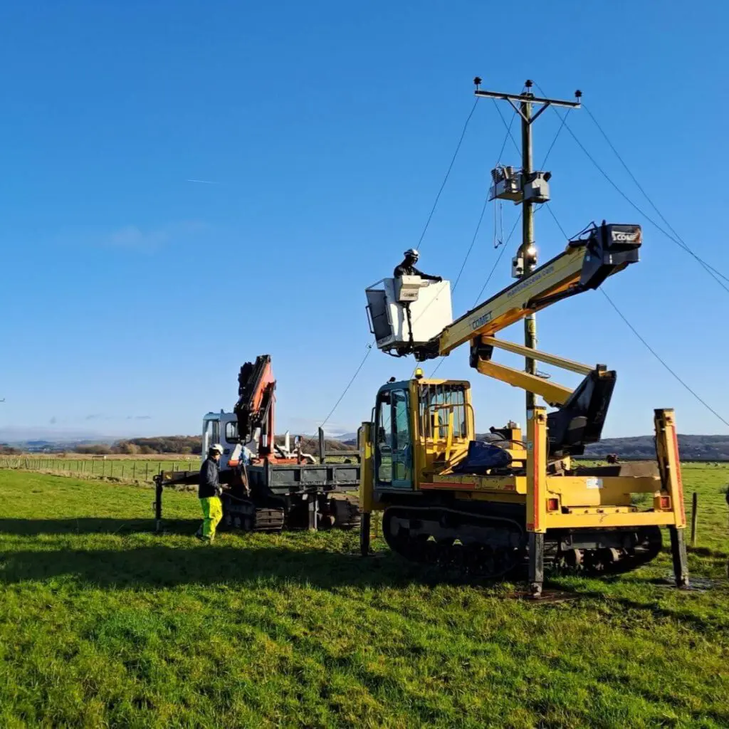A crane and people taking down electric cables in a field