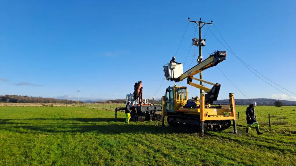 A crane and people taking down electric cables in a field