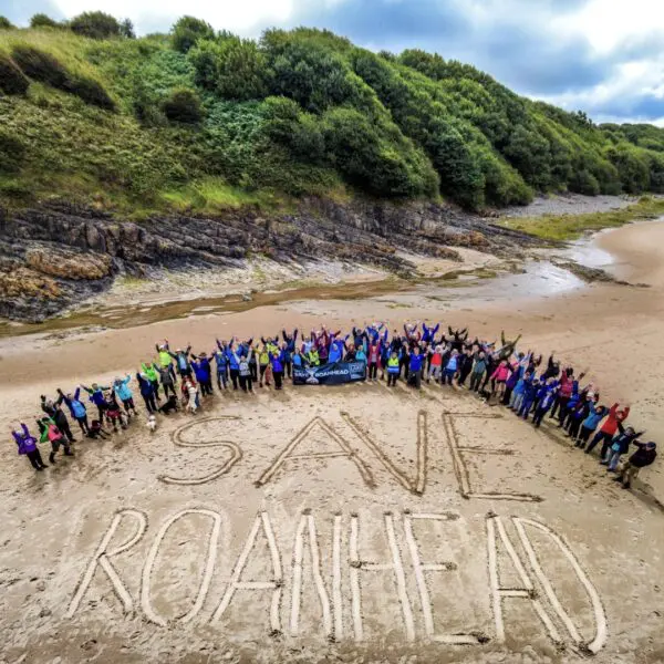 A group of protestors on a beach . They have written Save Roanhead on the sand.