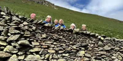 Some people peer up behind a dry stone wall