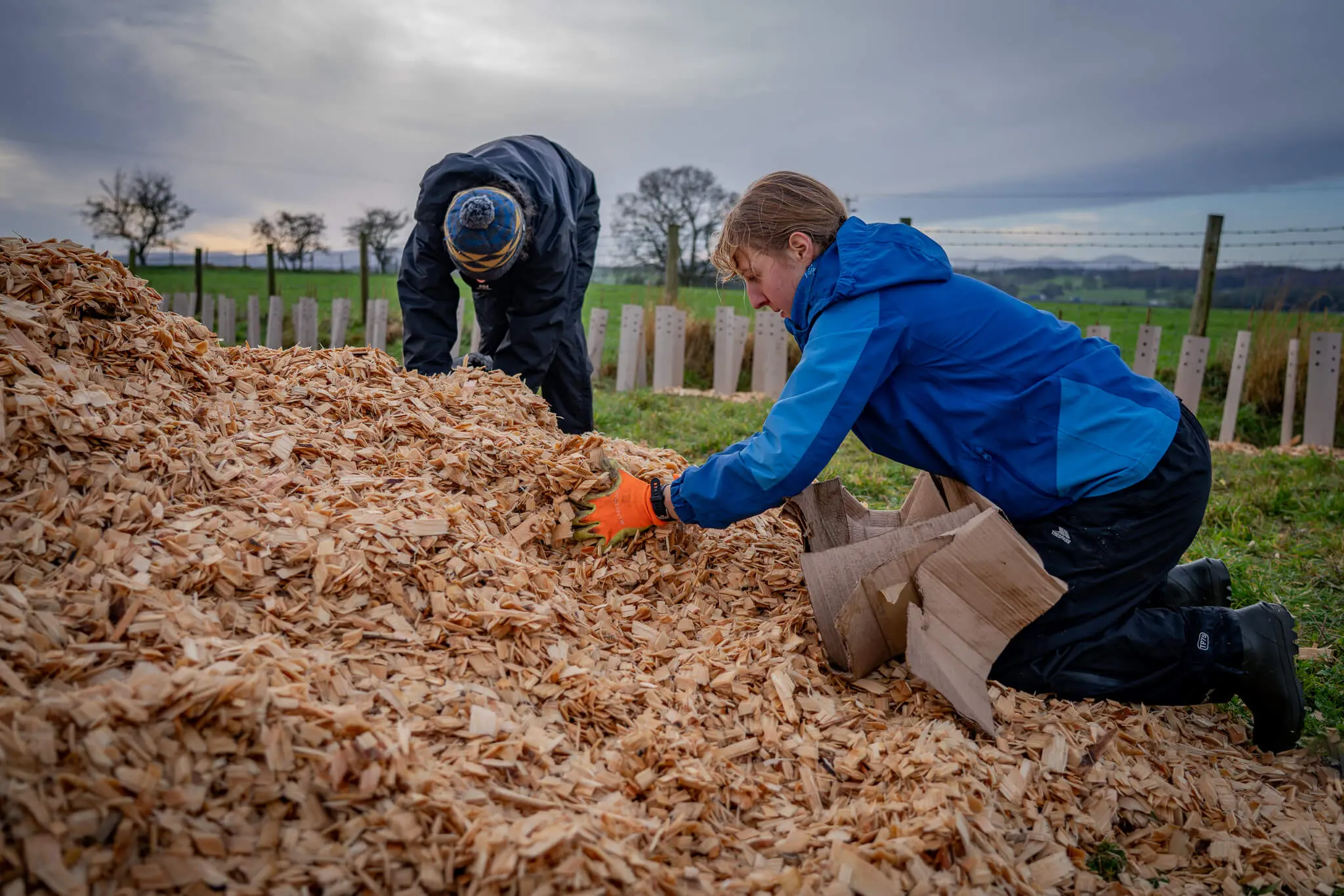 A student moving a pile of wood chippings