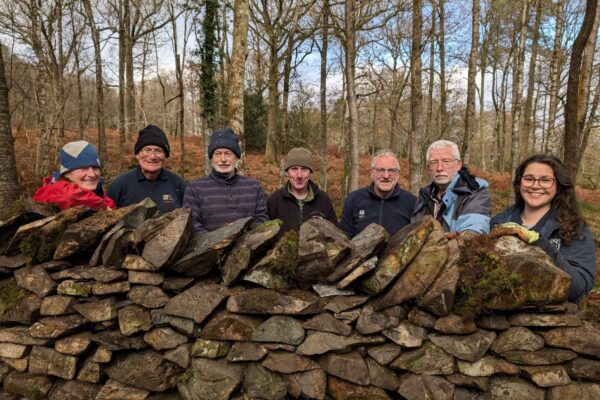 Dry stone walling volunteers stood behind a dry stone wall smiling