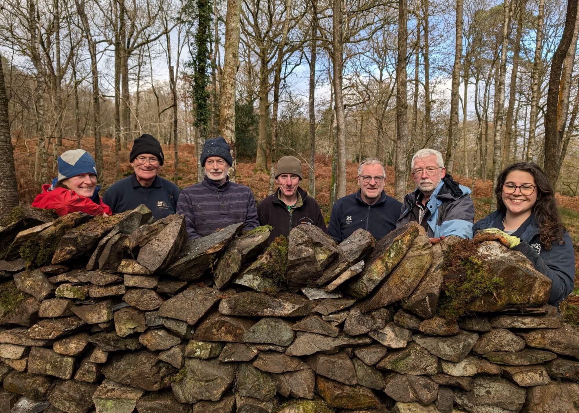 Dry stone walling volunteers stood behind a dry stone wall smiling